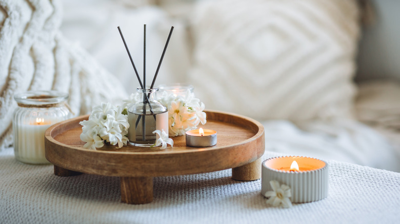 Aroma diffuser, candles, and white flowers on a wooden tray