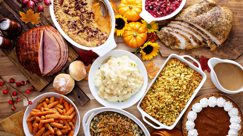 A Thanksgiving table loaded with turkey, ham, mashed potatoes, green bean casserole, roasted carrots, pumpkin pie, and more
