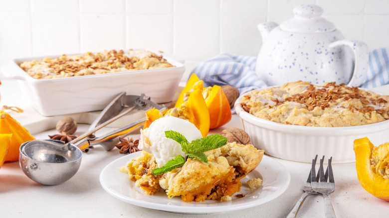 White dishes of pumpkin cobbler next to slices of pumpkin and silver utensils