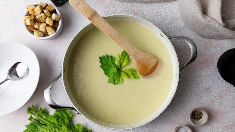 Pot of cream of celery soup with wooden spoon and bowl of croutons