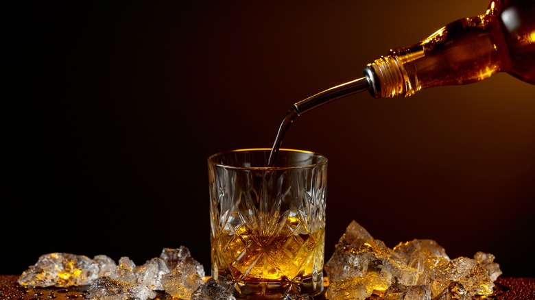 Whiskey being poured from a bottle into a glass surrounded by ice cubes