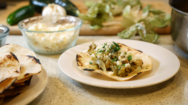 a verde chicken taco on a small plate beside tortillas, crumbled cheese, and vegetables