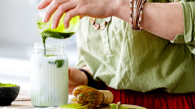 A person pouring matcha into a jar of milk