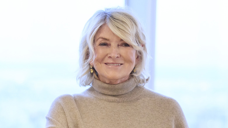 Smiling Martha Stewart in a beige turtleneck with a blurred glass background
