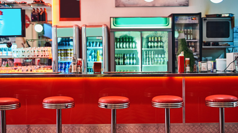 Counter and stools of a retro diner with coolers and drinks in the background