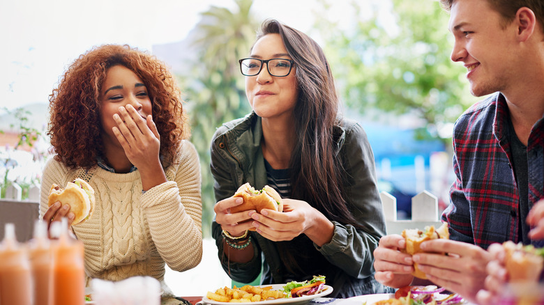 Cropped shot of three friends eating burgers outdoors