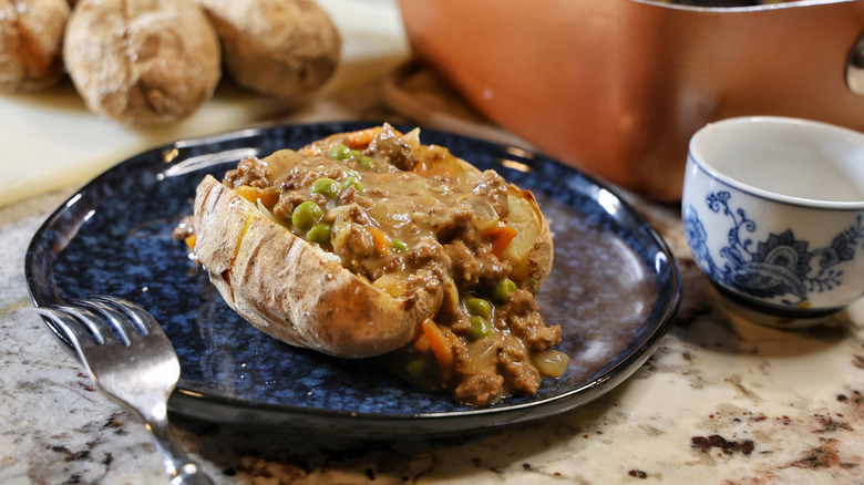 a split jacket potato filled with beef, vegetables, and gravy on a blue plate
