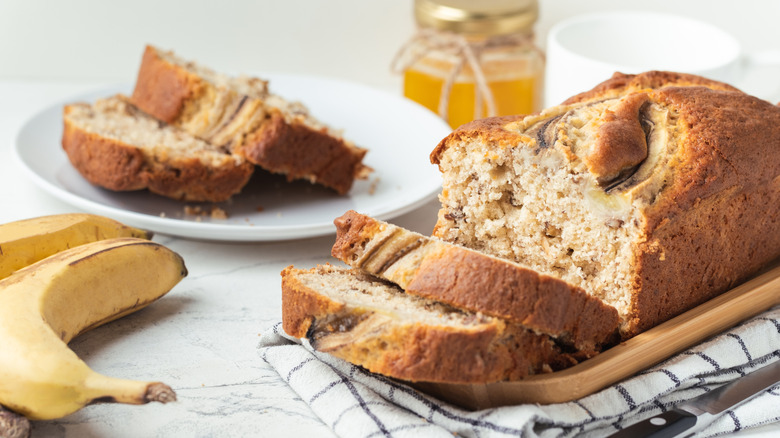 Banana bread on a wooden tray with a knife, bananas, and additional slices