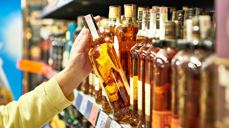 A person picking a bottle of whiskey off the shelf amidst a wide selection of bottles