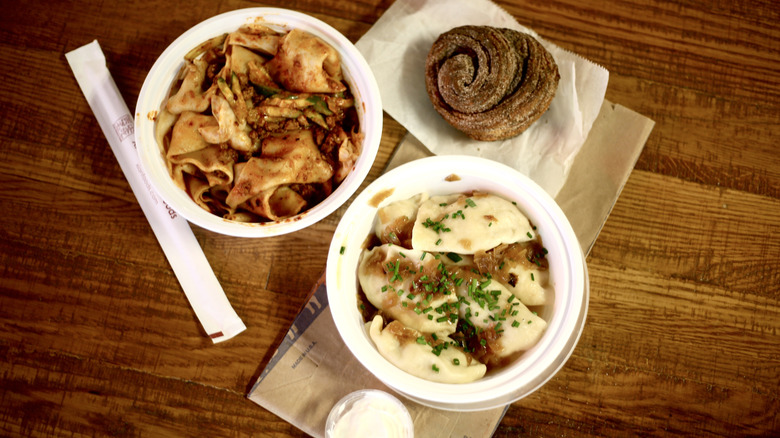 Swirled bun, pierogi, and noodles on a wooden table with napkins and chopsticks