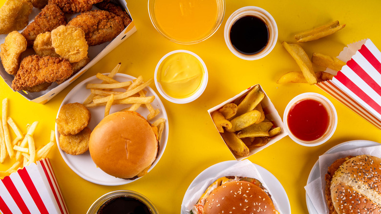 Assorted fast food sandwiches, fries, and sauces on yellow table