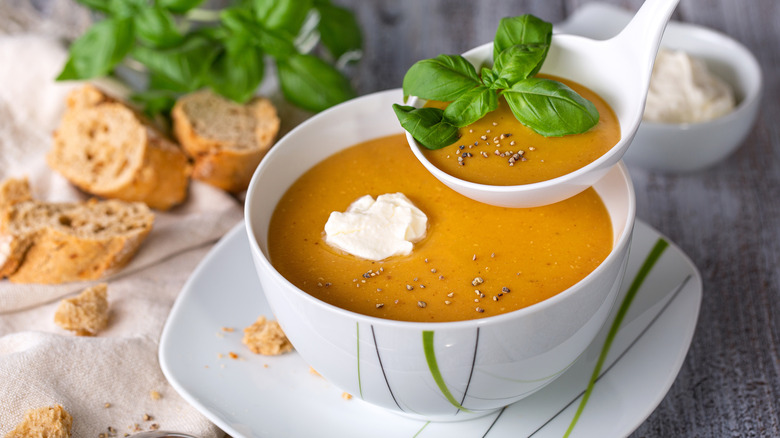 A bowl of lentil soup with a sprig of parsley sits on a white plate along with two pieces of multigrain toast.