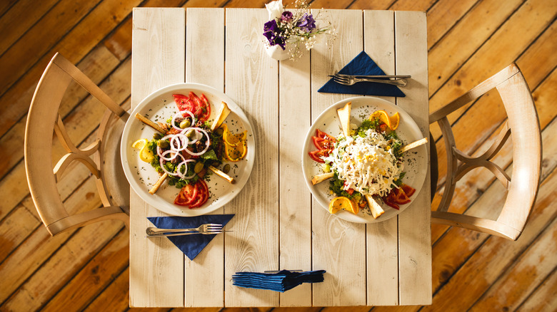 A top view of a rustic white table and chairs with Greek salads