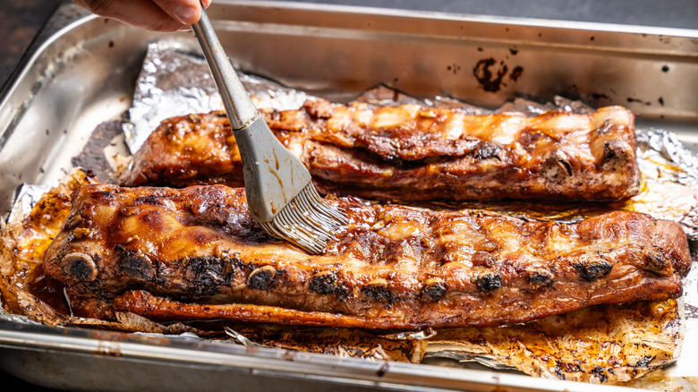 Someone brushes sauce on ribs on a piece of foil