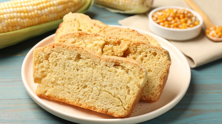 slices of cornbread cut from loaf on white plate with corn on cob and bowl of kernels