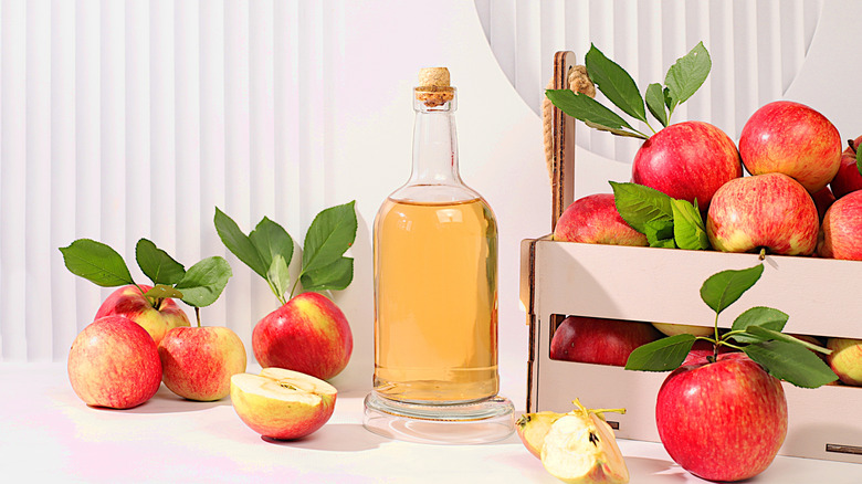 Apple cider in glass bottle surrounded by apples