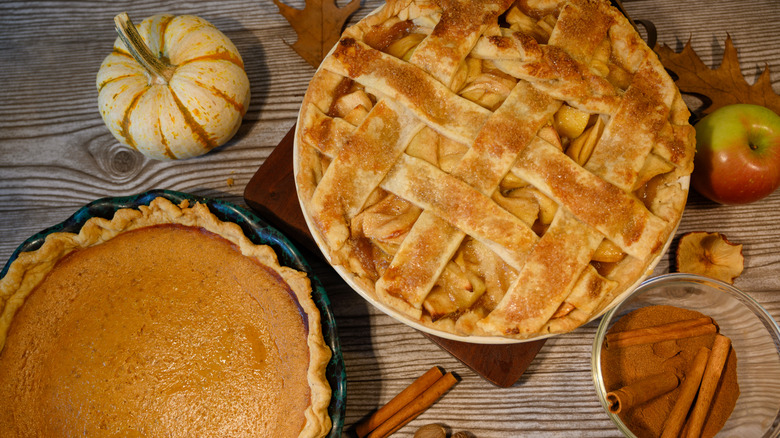 An apple pie and pumpkin pie sitting on a table