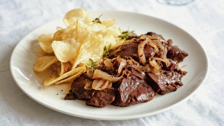 plate of beef liver and caramelized onions with potato chips