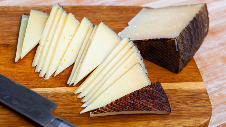 Semi-hard Manchego cheese slices on a wooden cutting board