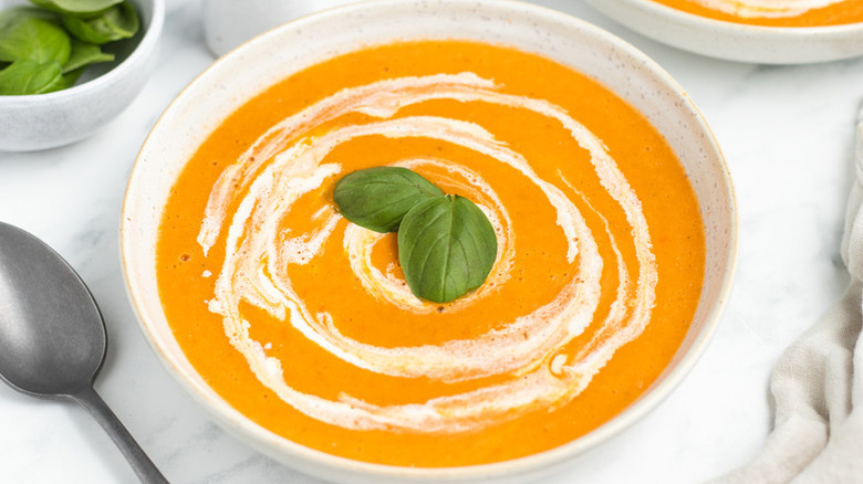 Bowl of roasted tomato soup, garnished with cream and fresh basil leaves