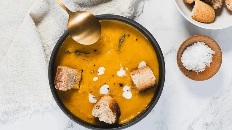 Carrot apple soup in bowl topped with chunks of bread and dollops of sour cream