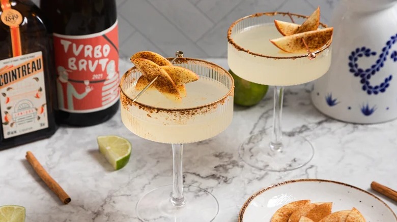Apple cider margaritas in glasses with skewered apple slices on marble counter