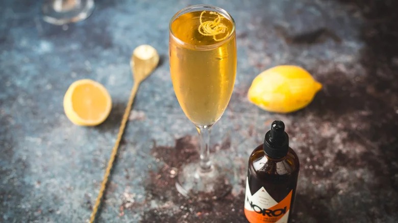 Smoky French 75 cocktail with bitters, lemon, bar spoon on dark table