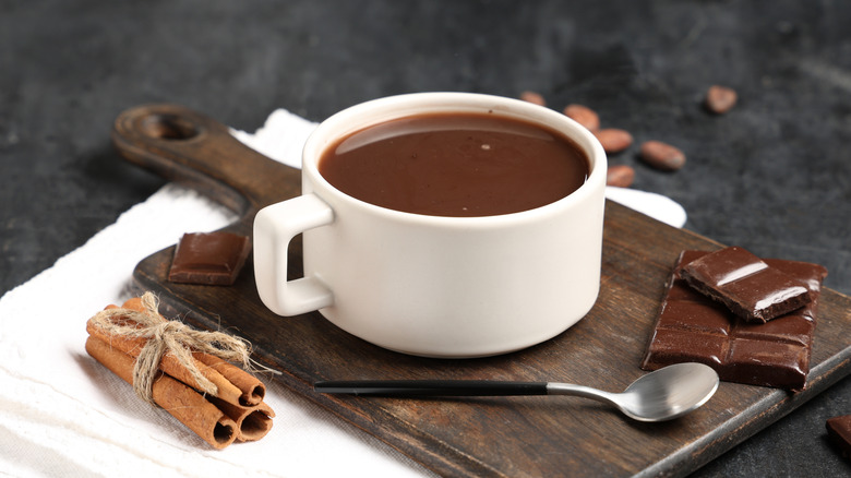 Wooden board with cup of tasty hot chocolate in a white mug with chocolate pieces on the side