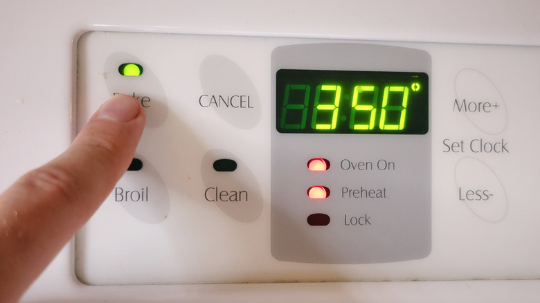 Finger pressing bake button on oven control panel