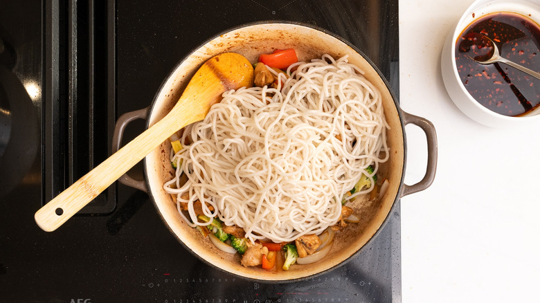 assembling noodle dish in pan