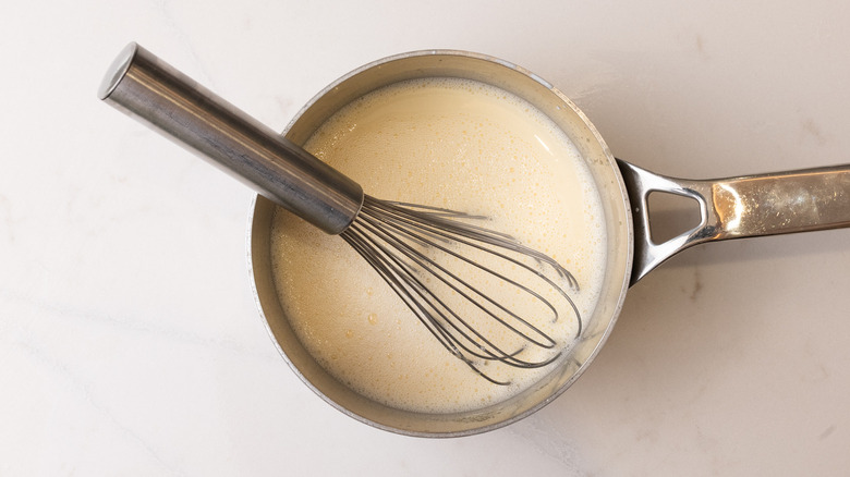 aerial view of saucepan with milk, custard mixture, and whisk