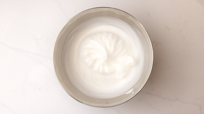 aerial view of stiff egg whites in mixing bowl on marble surface