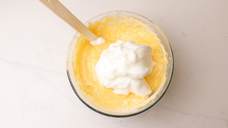 pile of egg whites sitting on top of cornmeal in glass bowl with spatula