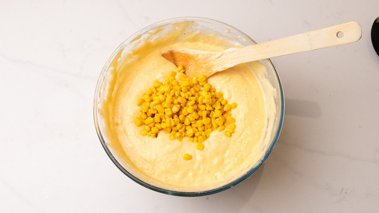 pile of corn sitting on top of unbaked souffle batter with spatula in the bowl