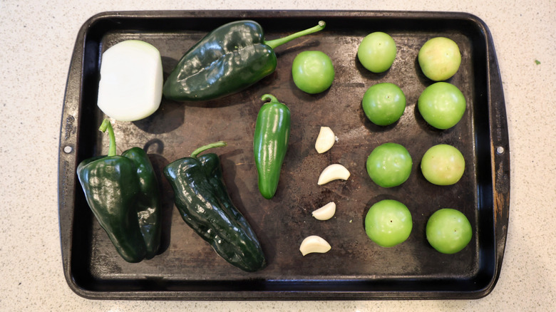 peppers, garlic, onion, and tomatillos arrayed on a baking sheet