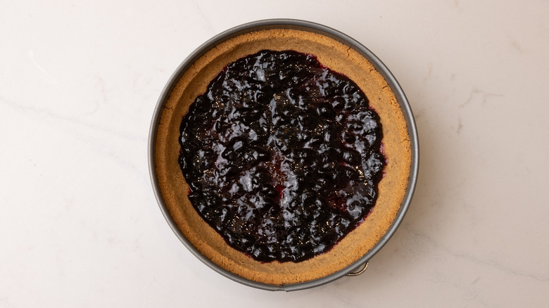 pie crust containing blueberry jam on the bottom in cake pan