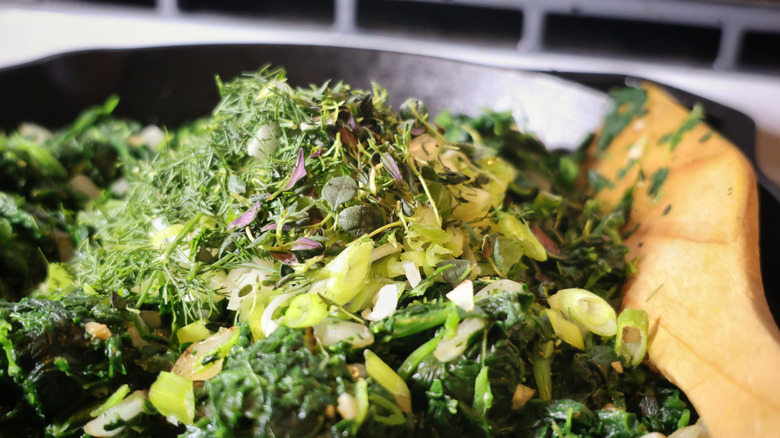 close-up of pile of fresh herbs on top of a skillet full of spinach