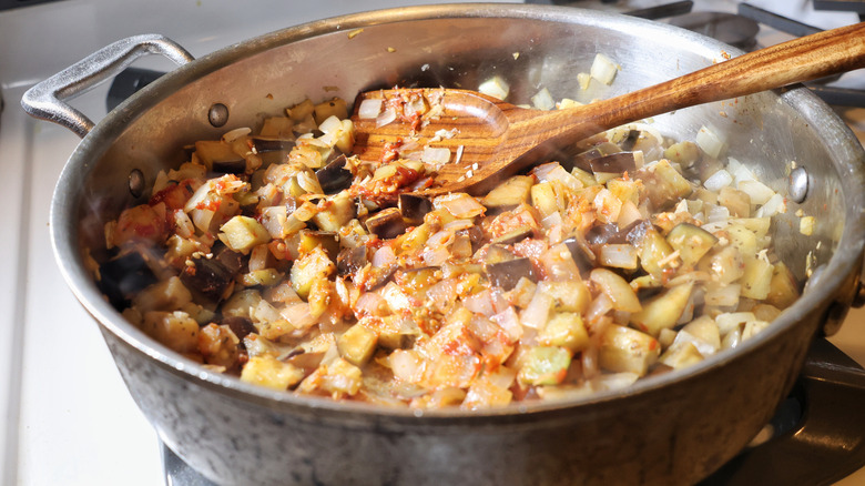 stainless steel pan of eggplant, onion, and garlic with wooden spatula in it