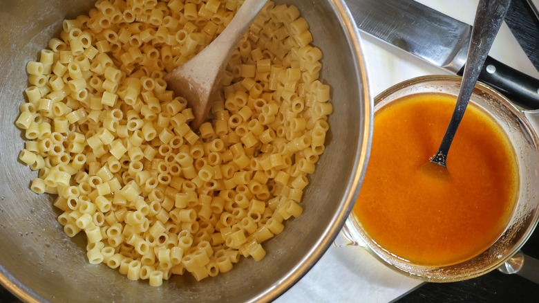 mixing bowl of ditalini pasta beside glass dish of reddish dressing