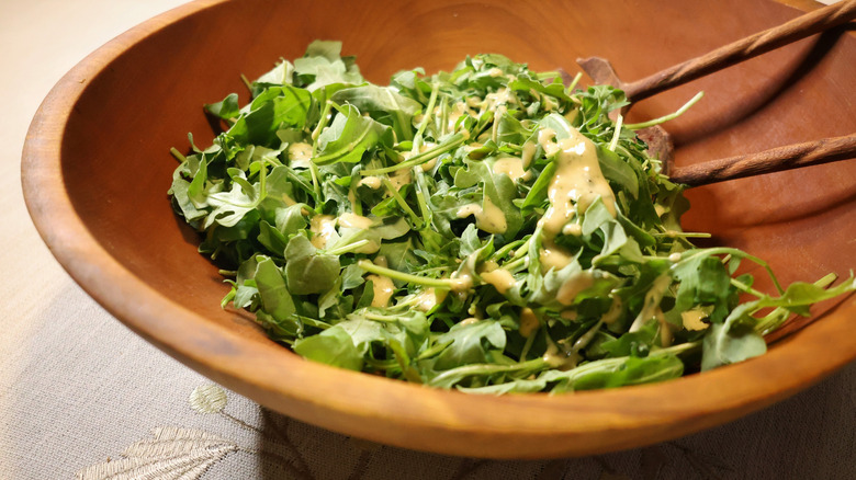 a wooden salad bowl of baby arugula topped with vinaigrette