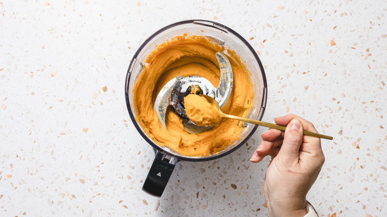 Hand lifting a spoon of orange batter from food processora