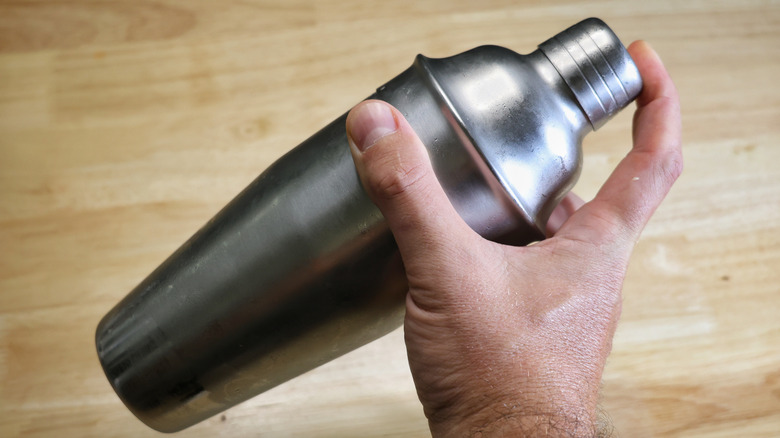hand holding metal cocktail shaker above wooden table
