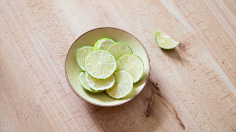 lime slices in shallow dish with a wedge of lime on a wooden surface