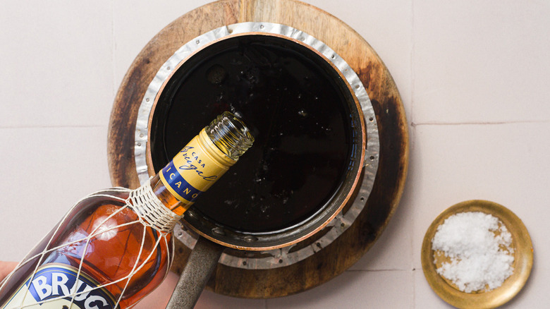 Adding rum to a saucepan of brown sugar syrup next to a bowl of salt