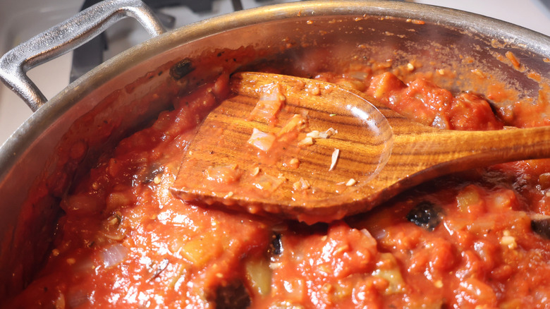 wooden spatula resting atop skillet of eggplant, onion, and garlic in red sauce