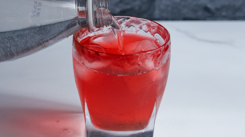 glass with red cocktail topped with soda water