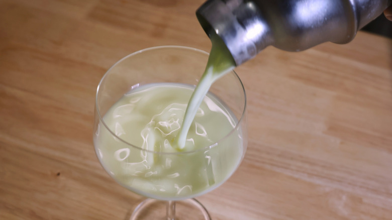 pale yellow cocktail pouring from cocktail shaker into coupe glass