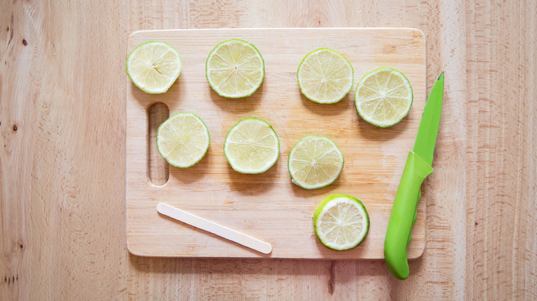 lime slices laid out on cutting board with popsicle stick and knife