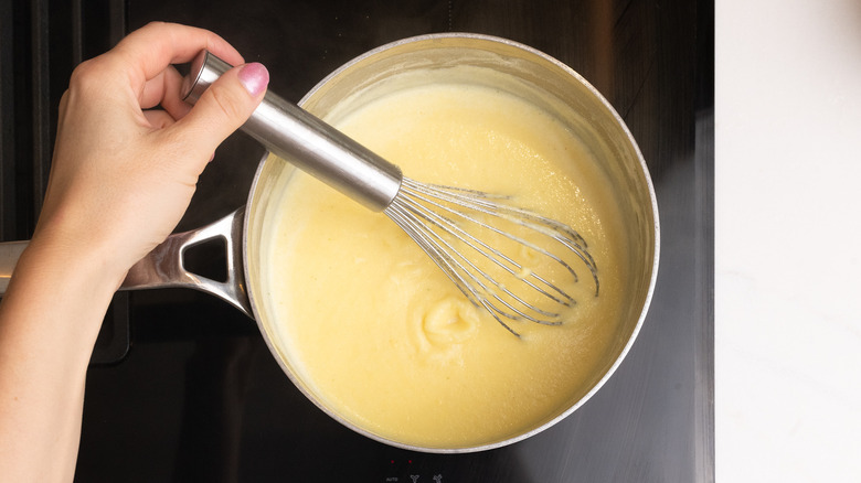 hand whisking cornmeal into pan with a whisk over stovetop