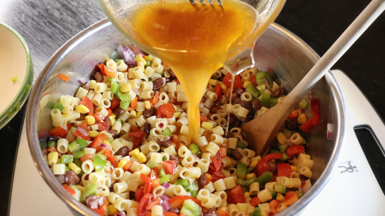dressing pouring into mixing bowl of cowboy caviar pasta salad